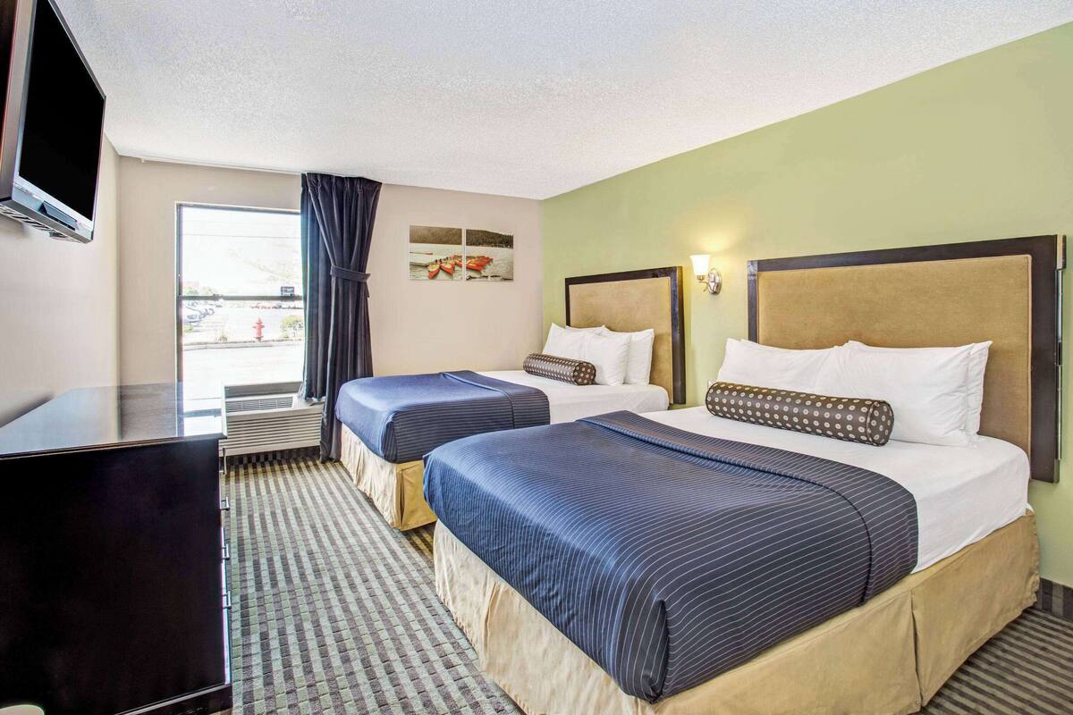 A hotel room with two beds, a flat-screen TV, a window with curtains, and artwork on the wall.