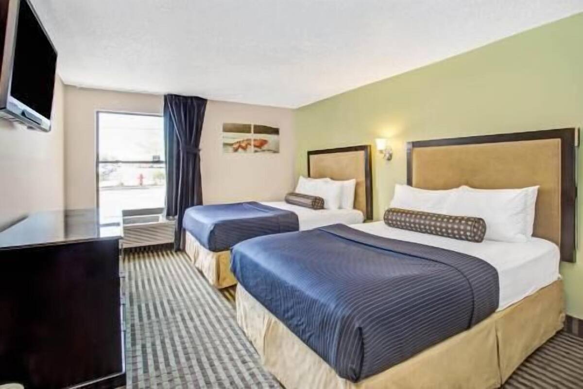 A hotel room with two beds, a television, a window with curtains, and a painting on the wall.