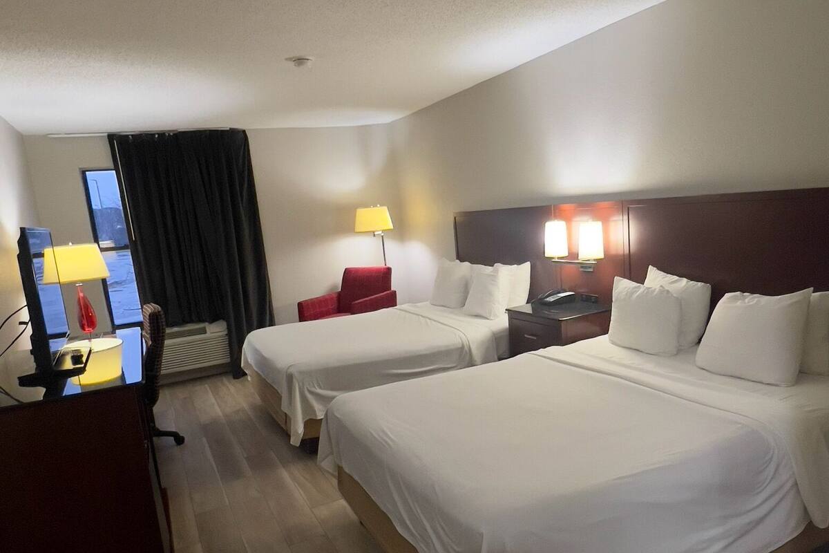 A hotel room with two beds, a desk, a chair, and a TV.