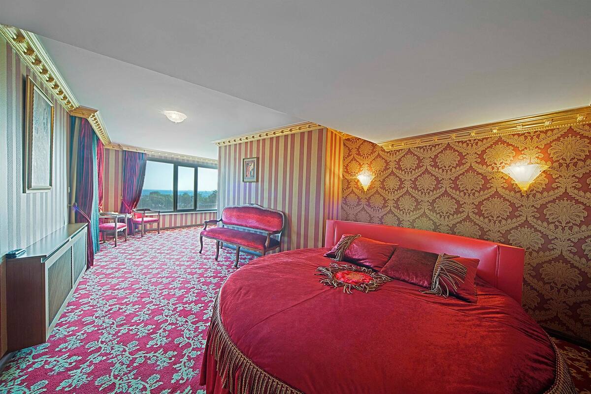 A hotel room with a large bed, a desk, a chair, and a view of the outdoors.