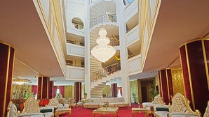 Un vestíbulo imponente con alfombra roja, muebles ornamentados y un candelabro central.