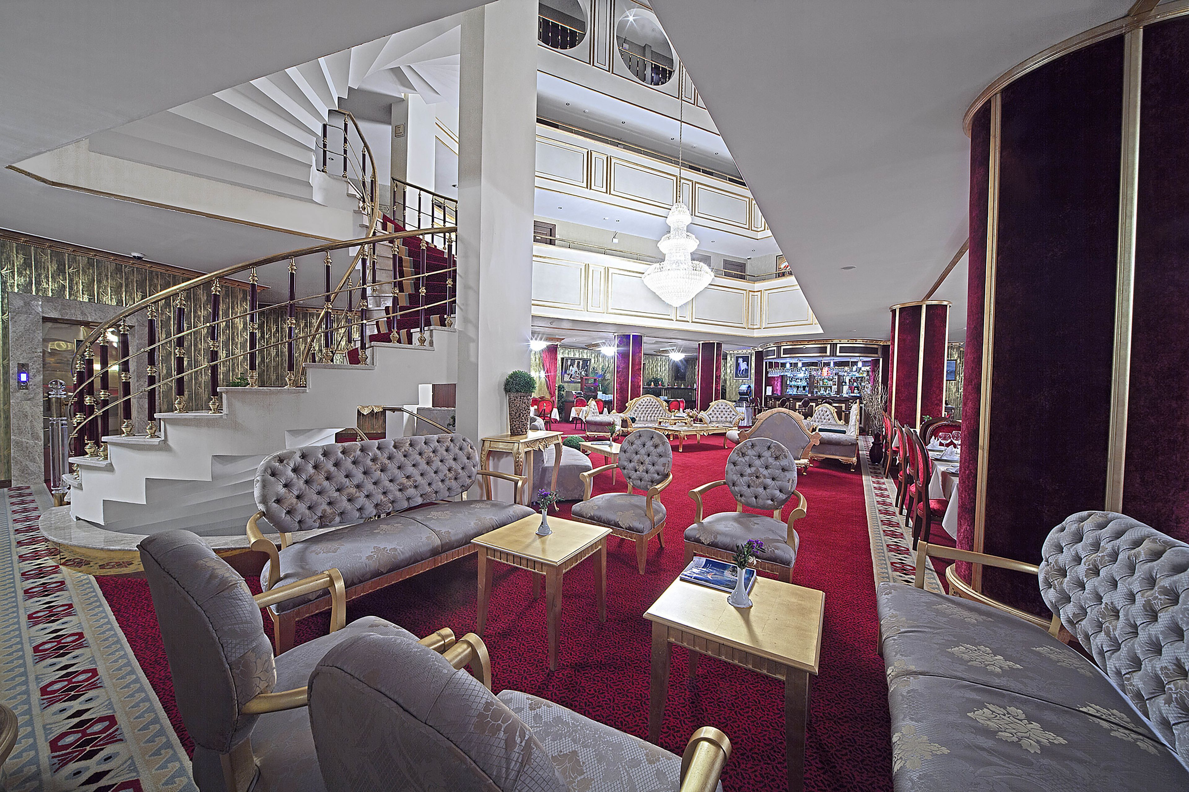 A spacious lobby with a grand staircase, plush seating, and a chandelier.