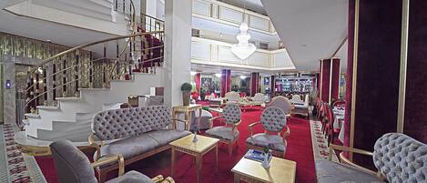 A spacious lobby with a grand staircase, plush seating, and a chandelier.