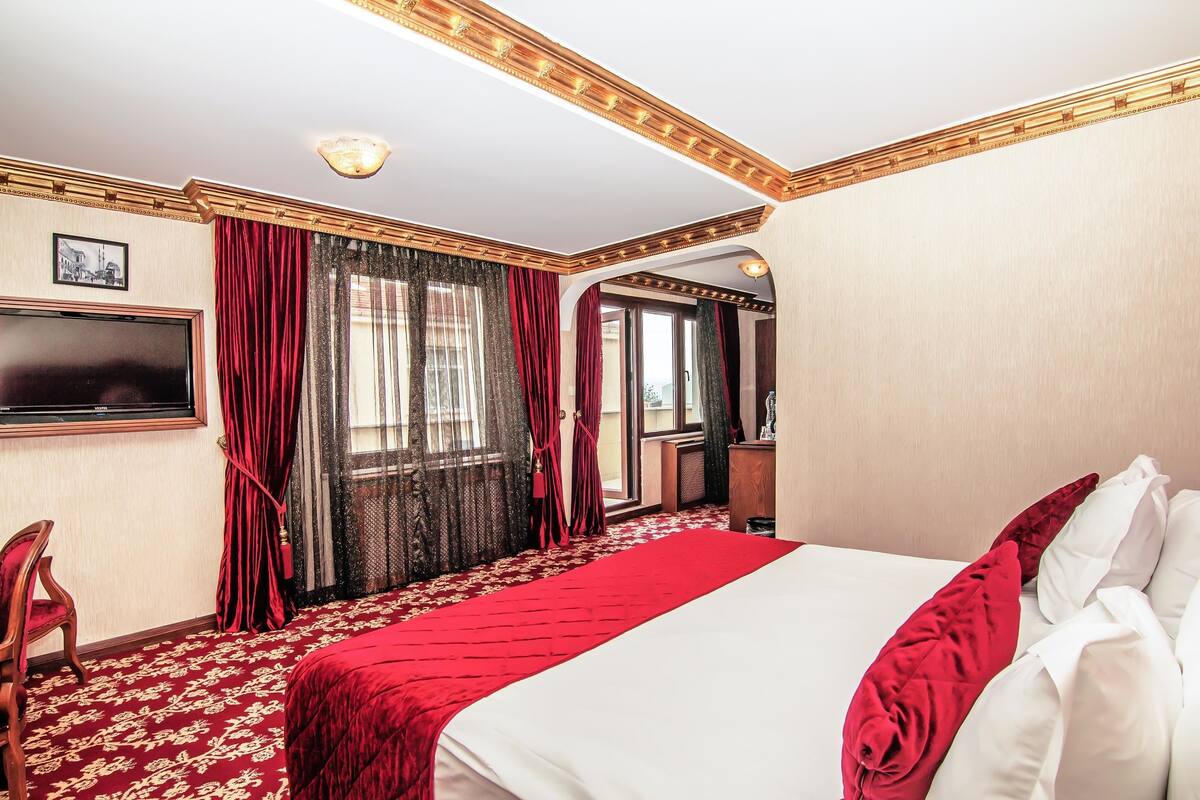 A hotel room with a large bed, a TV, a wooden chair, and a red carpet.