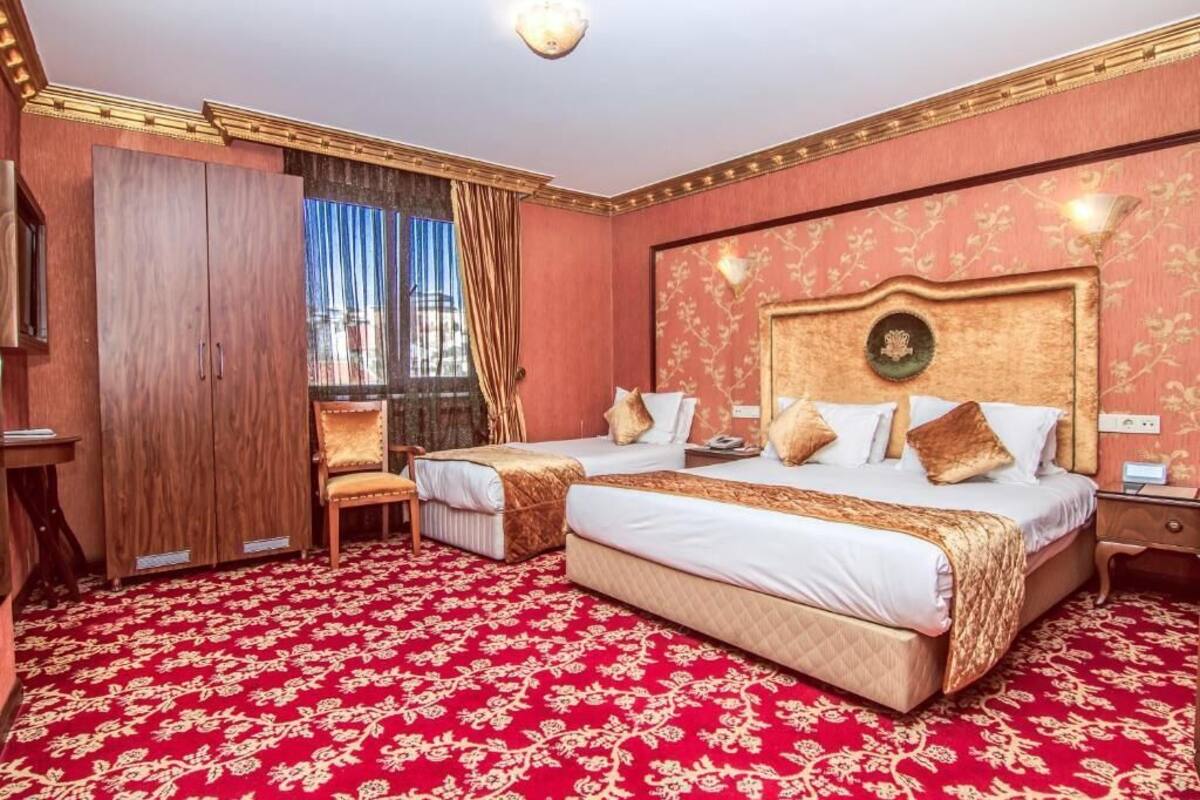 A hotel room with two beds, a wooden wardrobe, a chair, and a red carpeted floor.