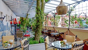 Un café al aire libre con mesas y sillas, un árbol grande y vistas de edificios a través de un techo de cristal.