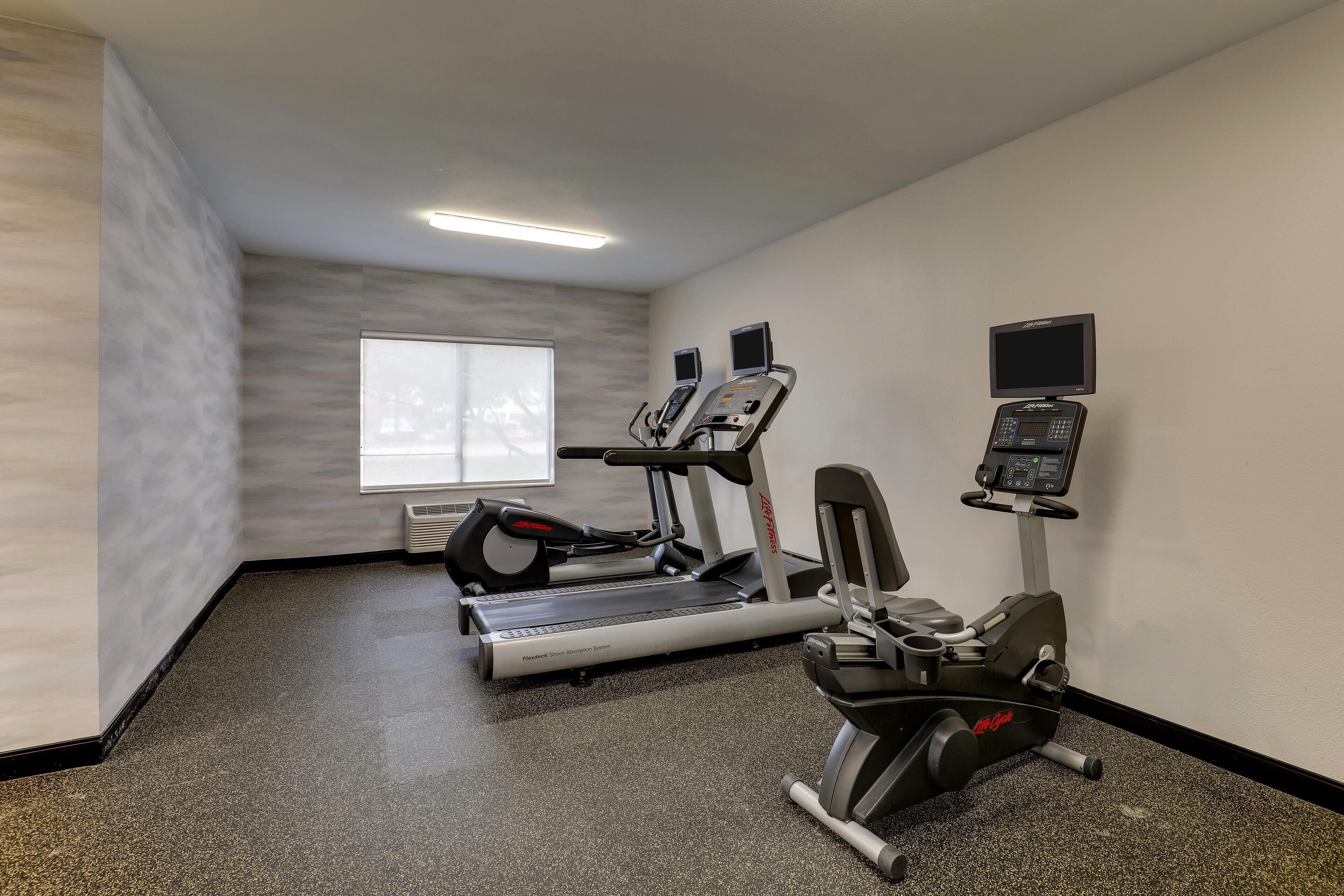 A gym with a treadmill, elliptical, and weight machine.