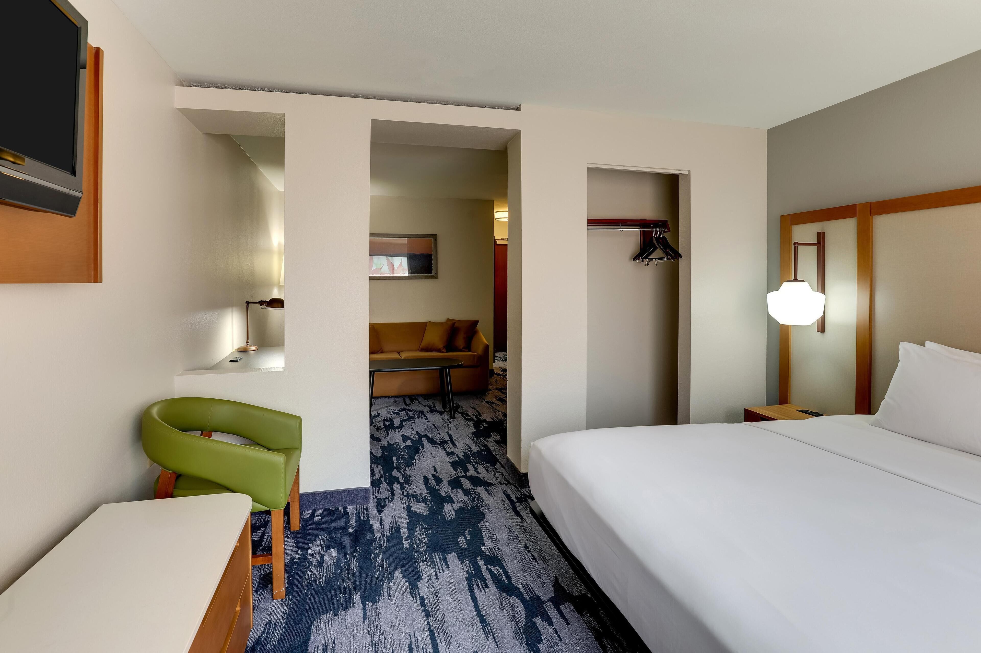 A hotel room with a bed, a green chair, a sofa, and a TV mounted on the wall.