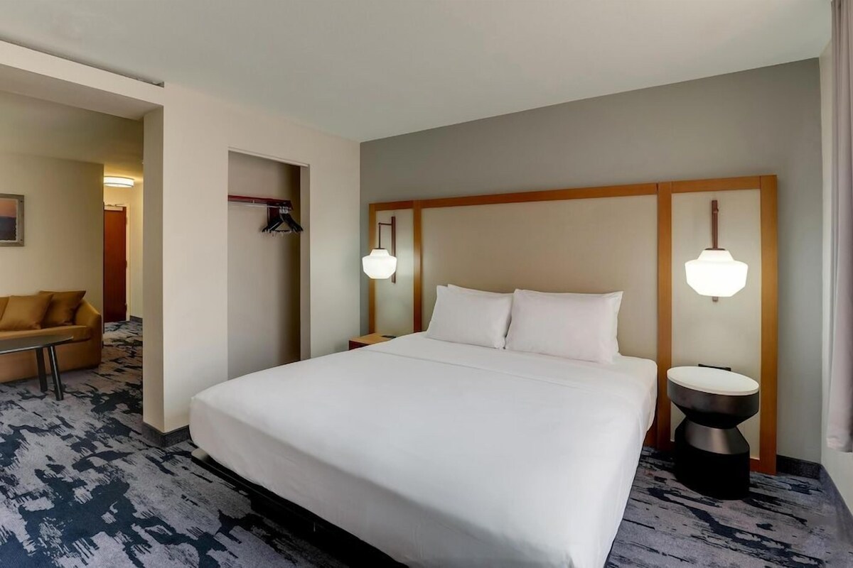 A hotel room with a large bed, two bedside tables, a chair, and a coat rack.