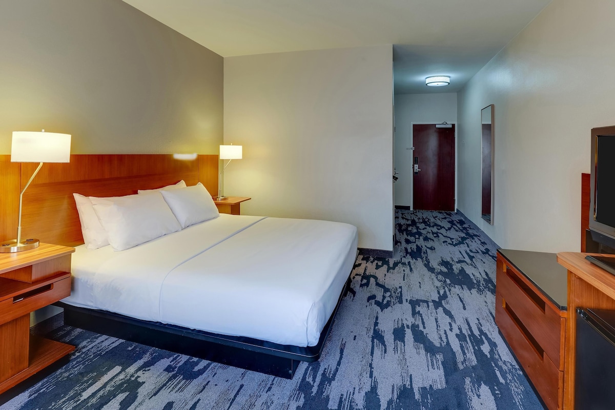 Habitación de hotel con una cama grande, dos lámparas de noche, cabecera de madera, televisor de pantalla plana y piso alfombrado.