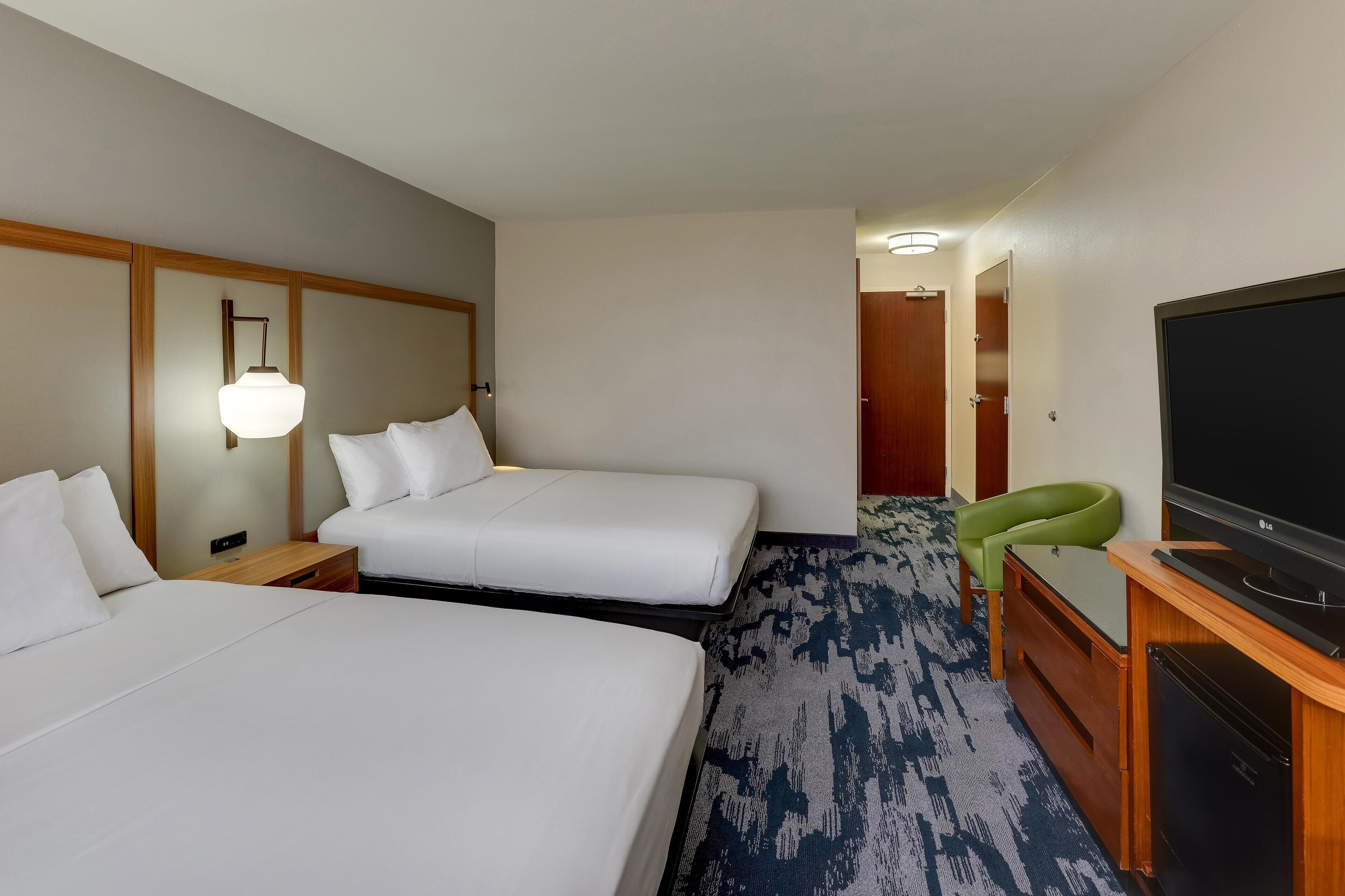 A hotel room with two beds, a desk with a television, and a green chair.