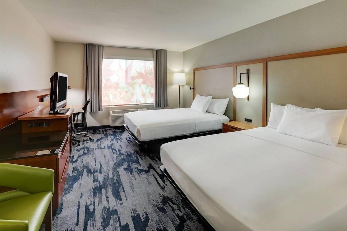 A hotel room with two beds, a desk, a television, and a window with curtains.