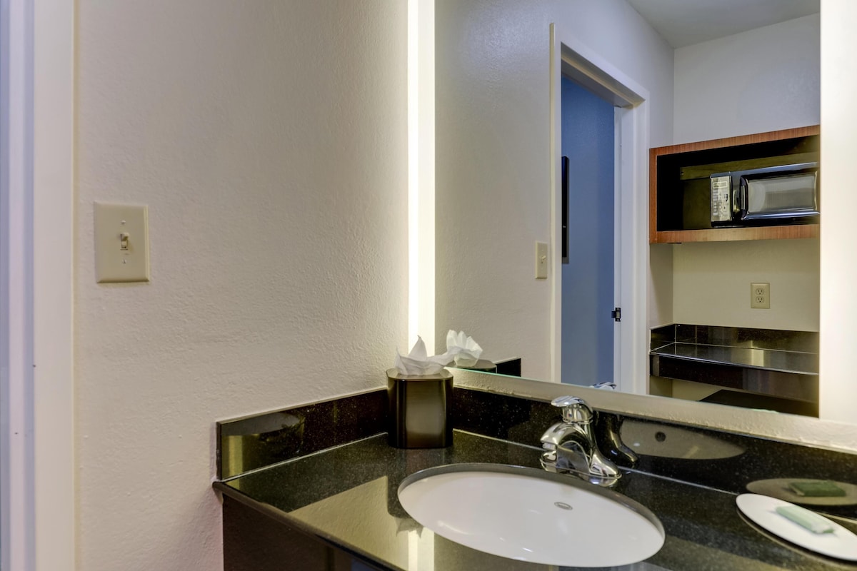 Un baño con un lavabo blanco, un espejo y un estante con artículos de tocador.