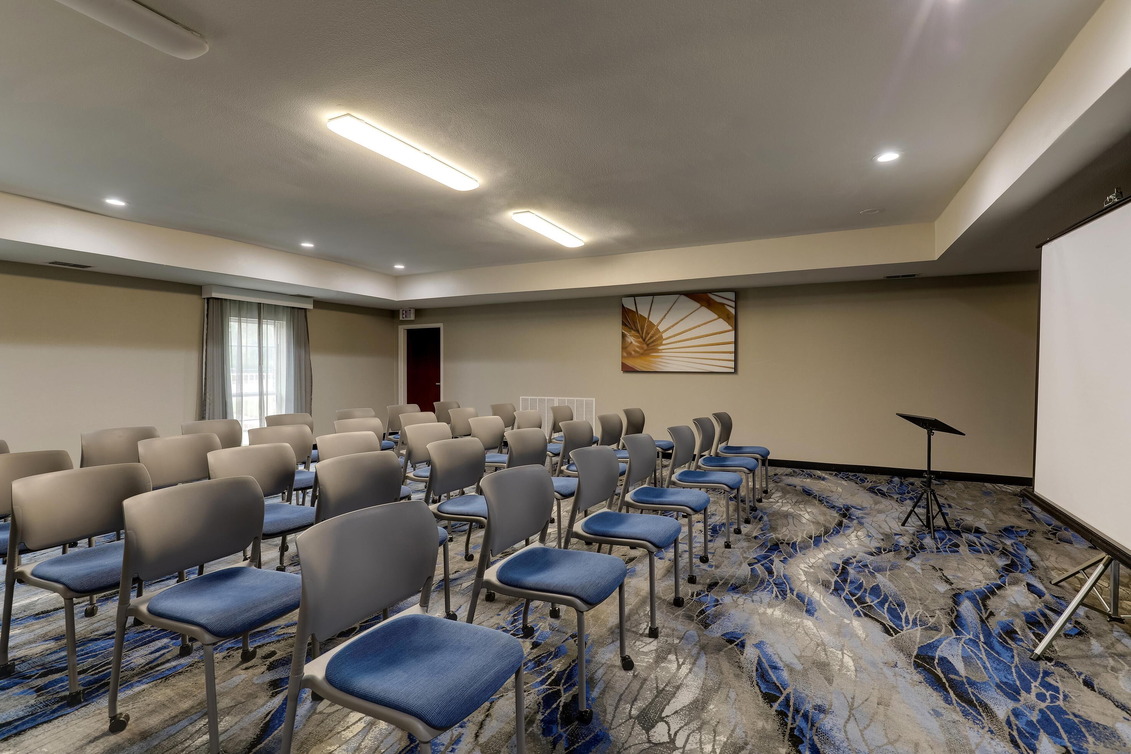 A conference room with rows of chairs, a projector screen, and a carpeted floor.