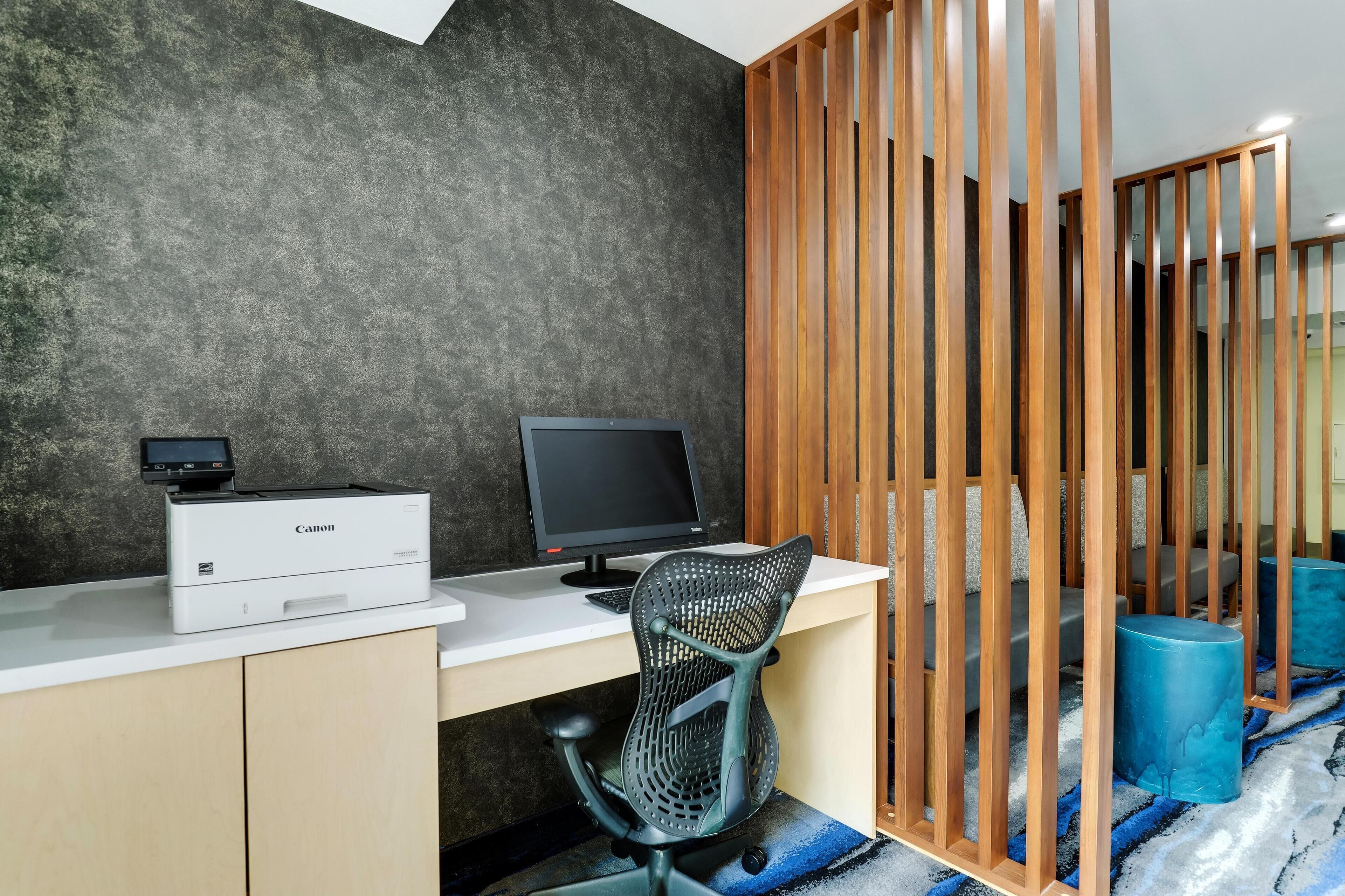 A modern office space with a white desk, a Canon printer, a black monitor, and a black mesh office chair.