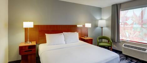 Habitación de hotel con una cama grande, dos mesitas de noche con lámparas, una silla verde, un ventanal con vistas y un aire acondicionado instalado en la pared.