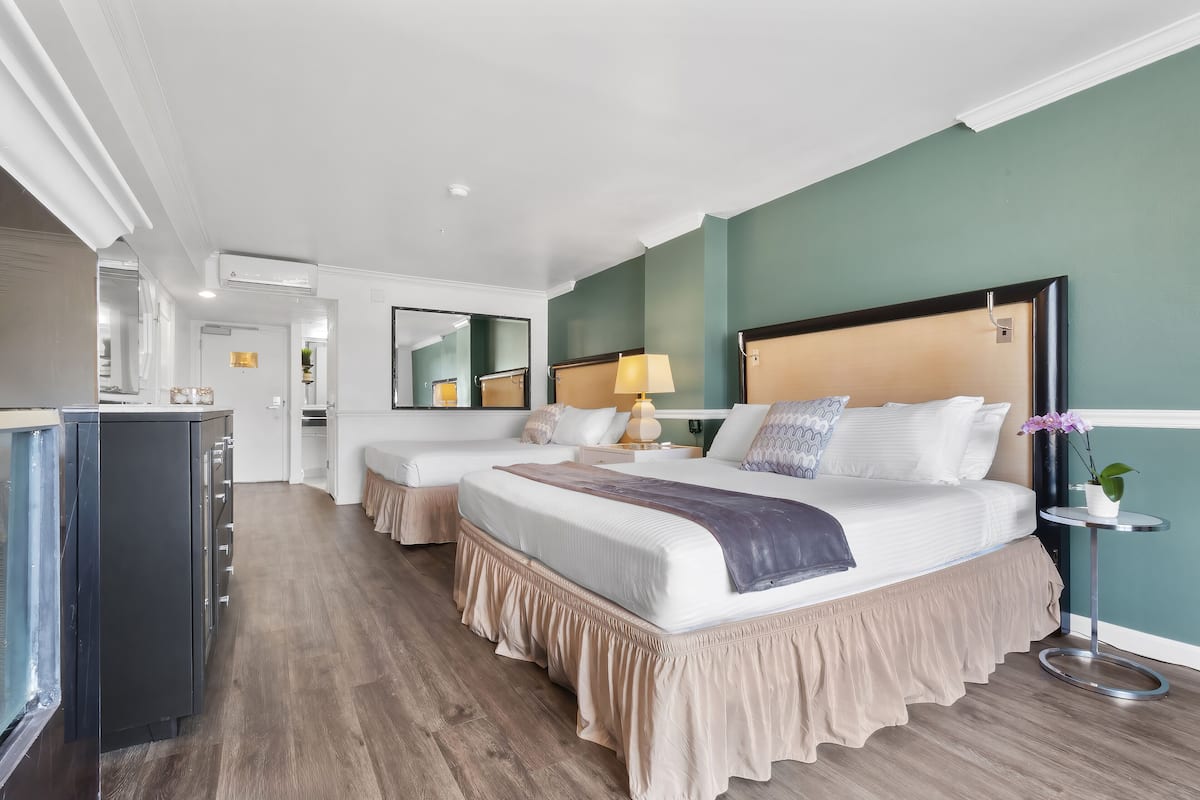 A hotel room with two beds, a minibar, a small table with a lamp, and a potted plant.