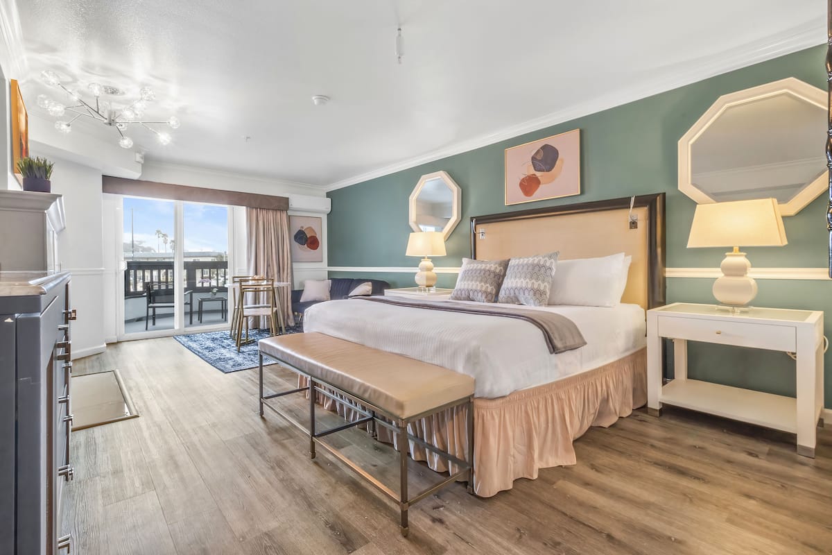 A spacious bedroom with a large bed, a bench, a desk, and a view of the outdoors.