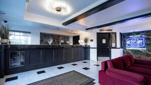 Un hall de hotel con una mesa de recepción, un sofá rojo y un letrero de neón que dice "Welcome ASCOT Suites".
