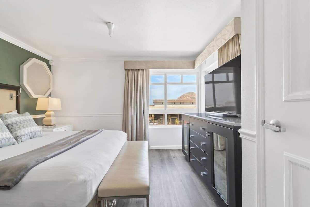 A hotel room with a bed, a bench, a TV, a dresser, and a window with a view.