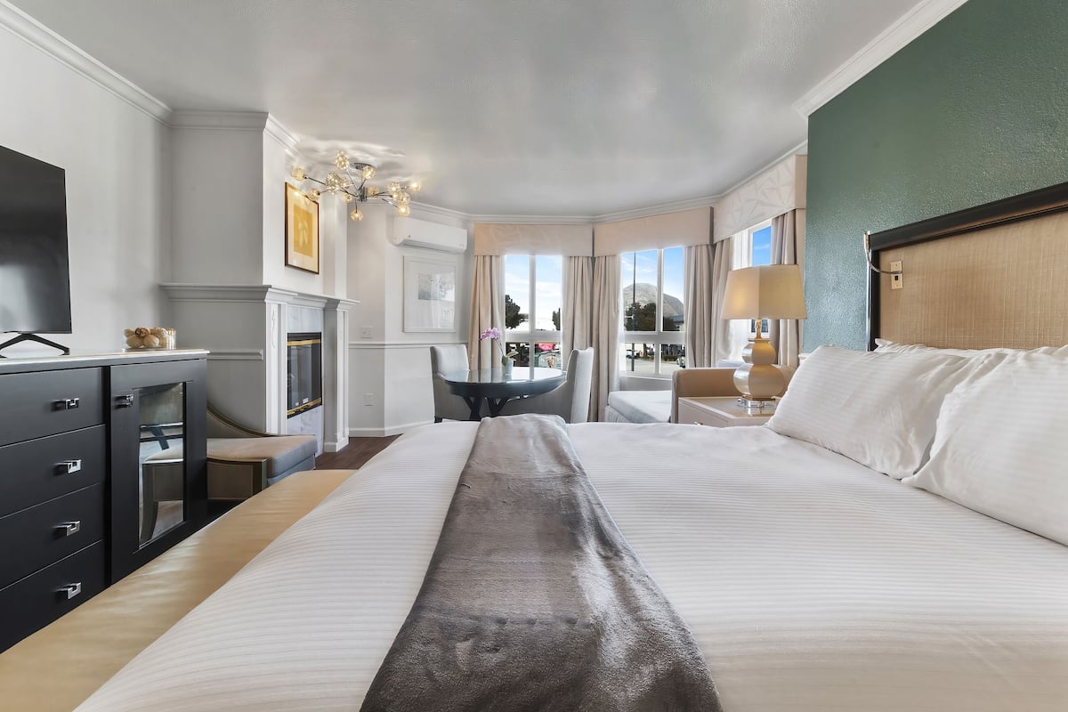 A hotel room with a large bed, a desk, a chair, a TV, and a fireplace.