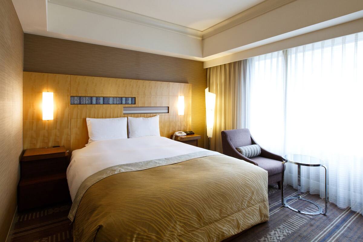Une chambre d’hôtel avec un grand lit, des tables de chevet, une chaise et une fenêtre avec des rideaux.