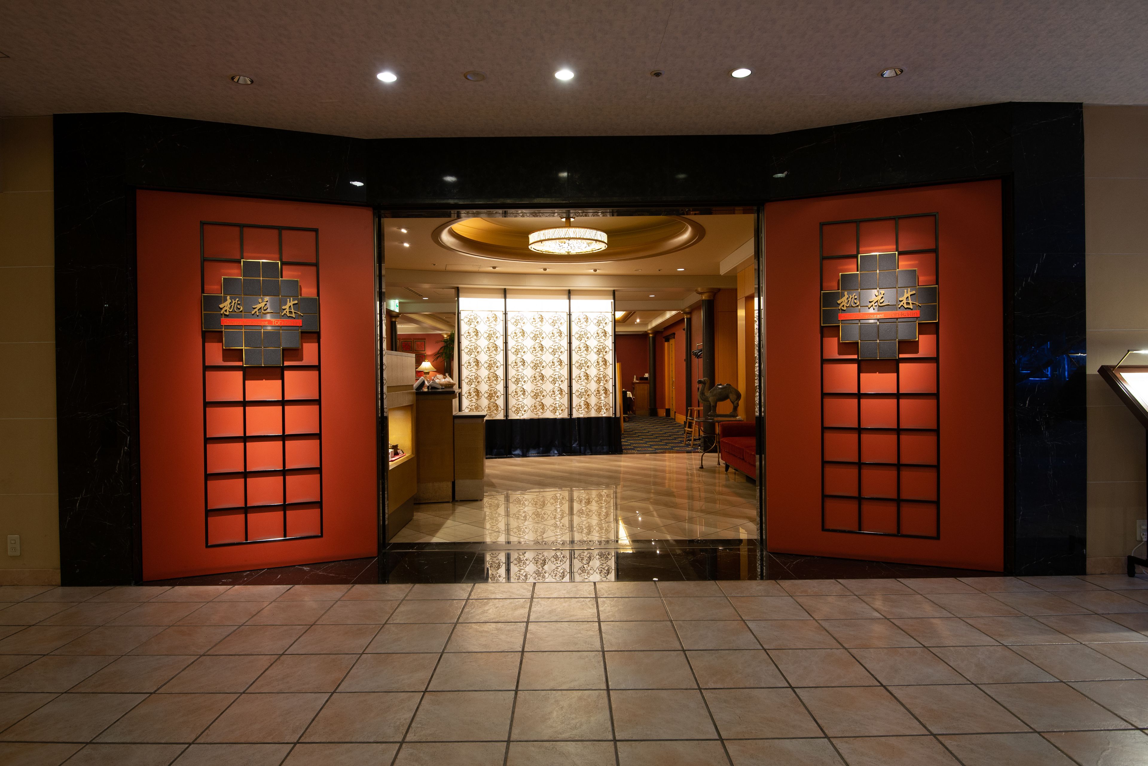 A hotel lobby with a modern design, featuring a reception desk, a chandelier, and a patterned wall.