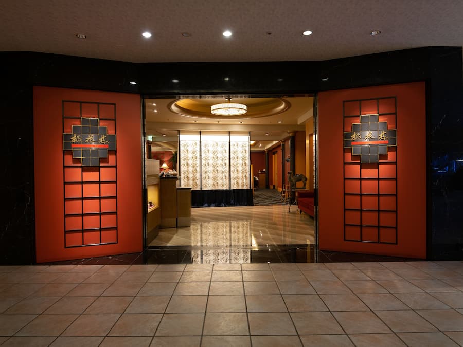 A hotel lobby with a modern design, featuring a reception desk, a chandelier, and a patterned wall.