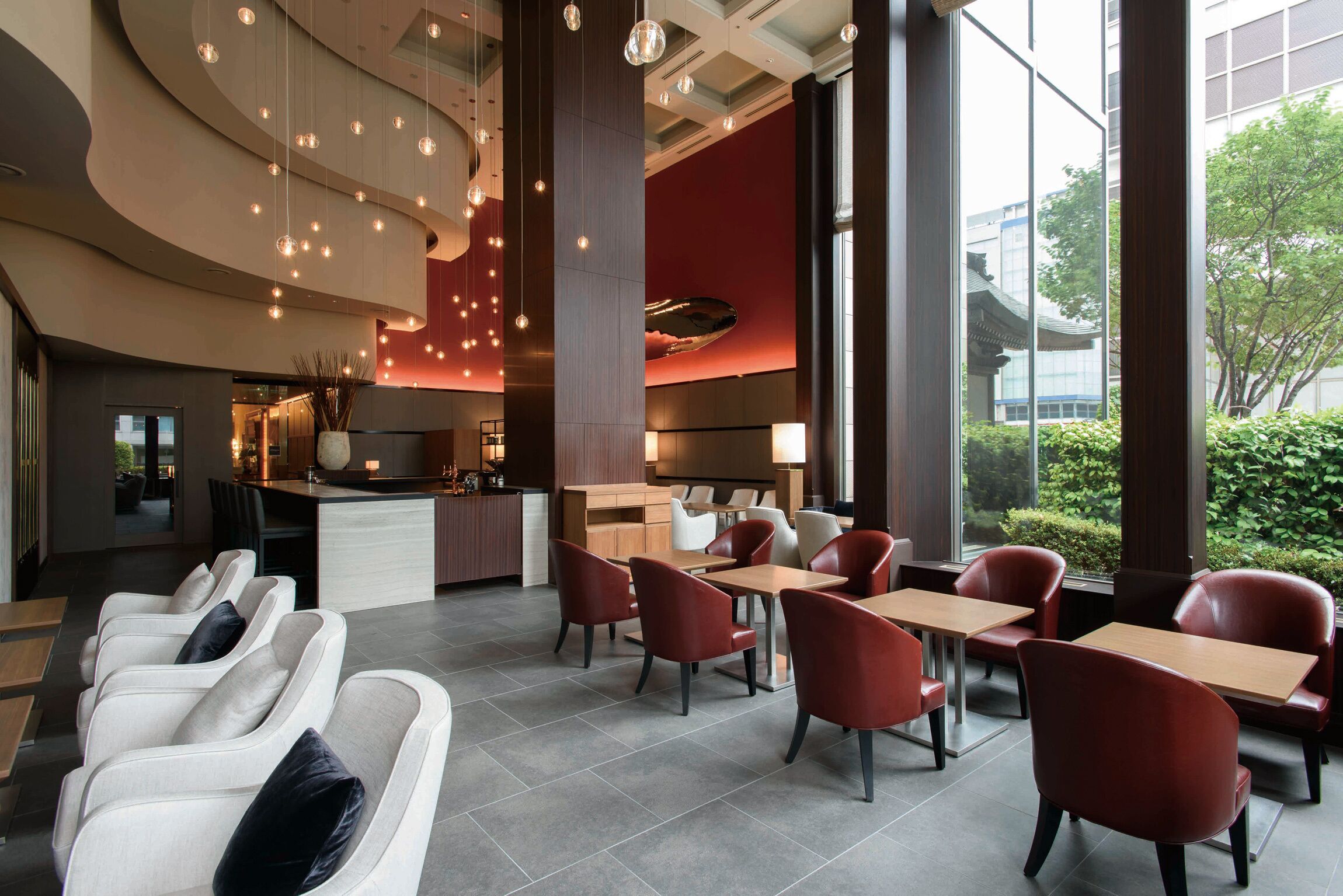 A modern hotel lobby with a reception desk, seating area, and large windows offering views of the outdoors.