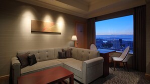 A hotel room with a sofa, a coffee table, a desk, and a chair. There is a large window with a city view. - Hotel Okura Fukuoka (Fukuoka)