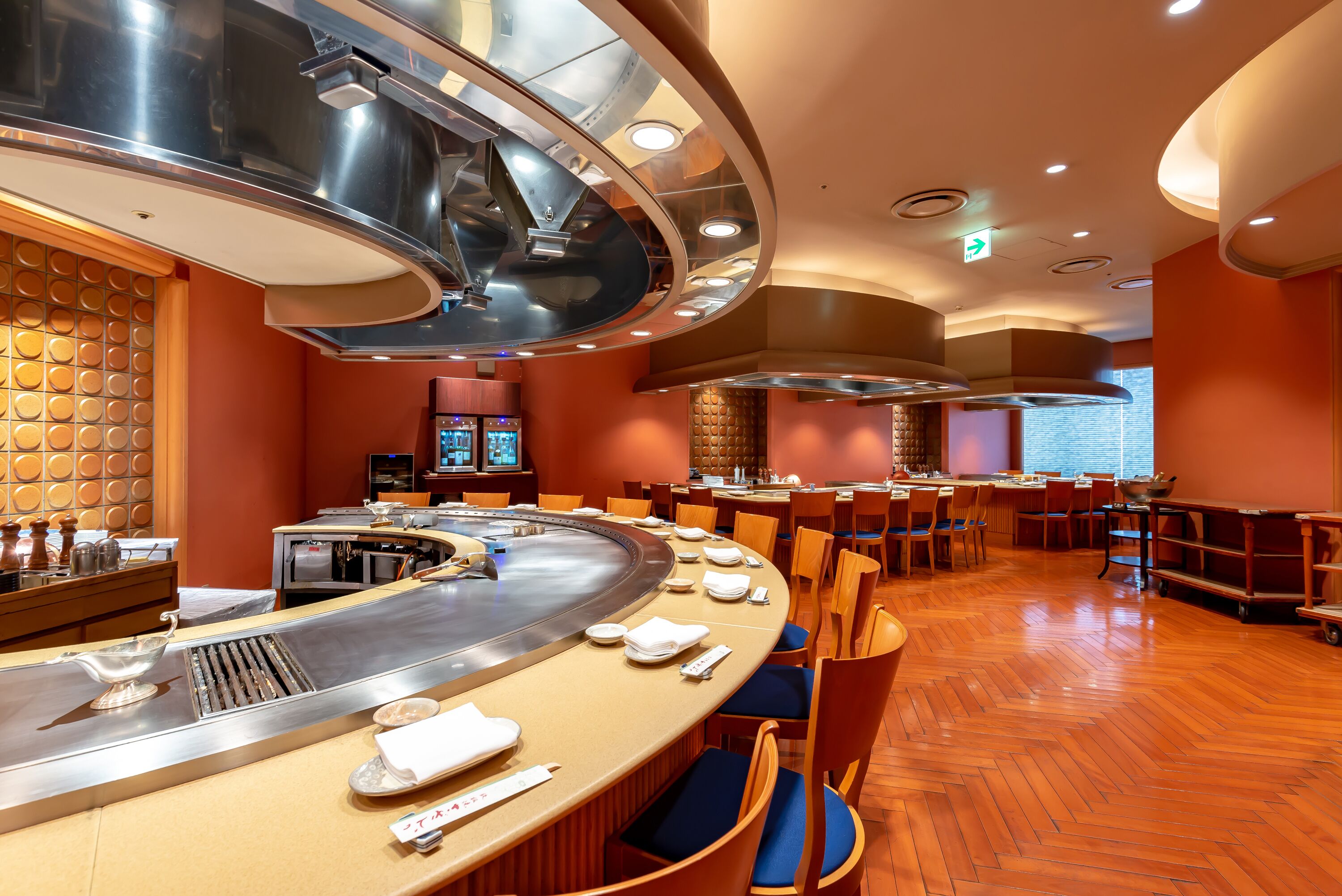 A restaurant with a sushi bar, wooden flooring, and a modern interior design.