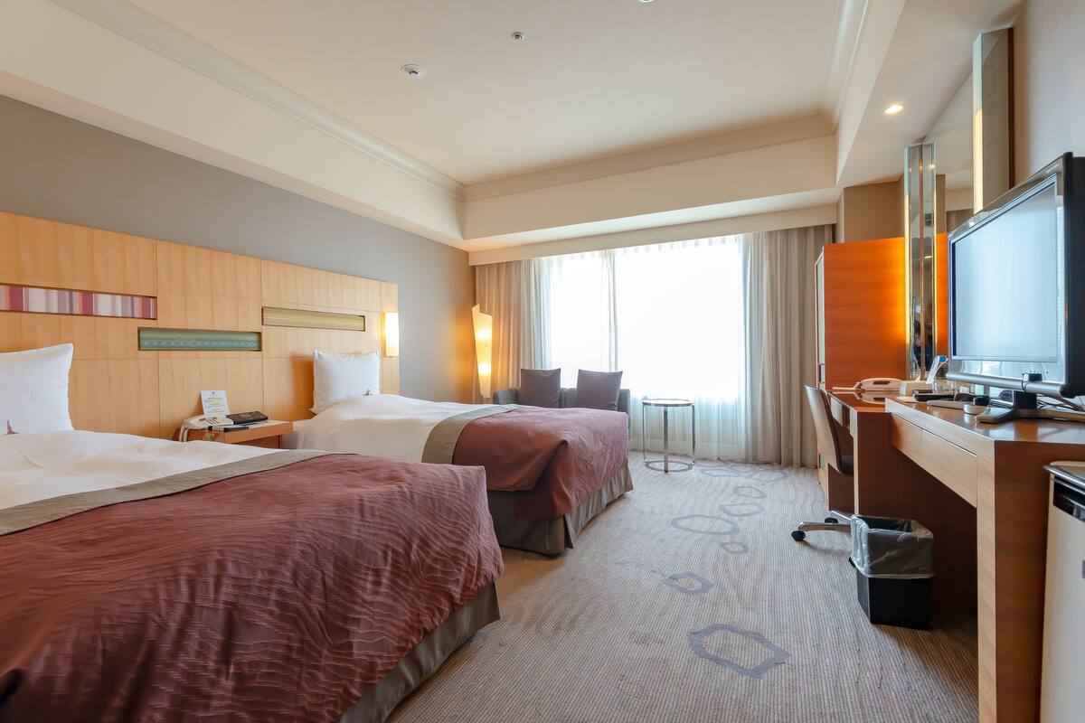 Une chambre d’hôtel avec deux lits, un bureau, une télévision et une fenêtre avec des rideaux.