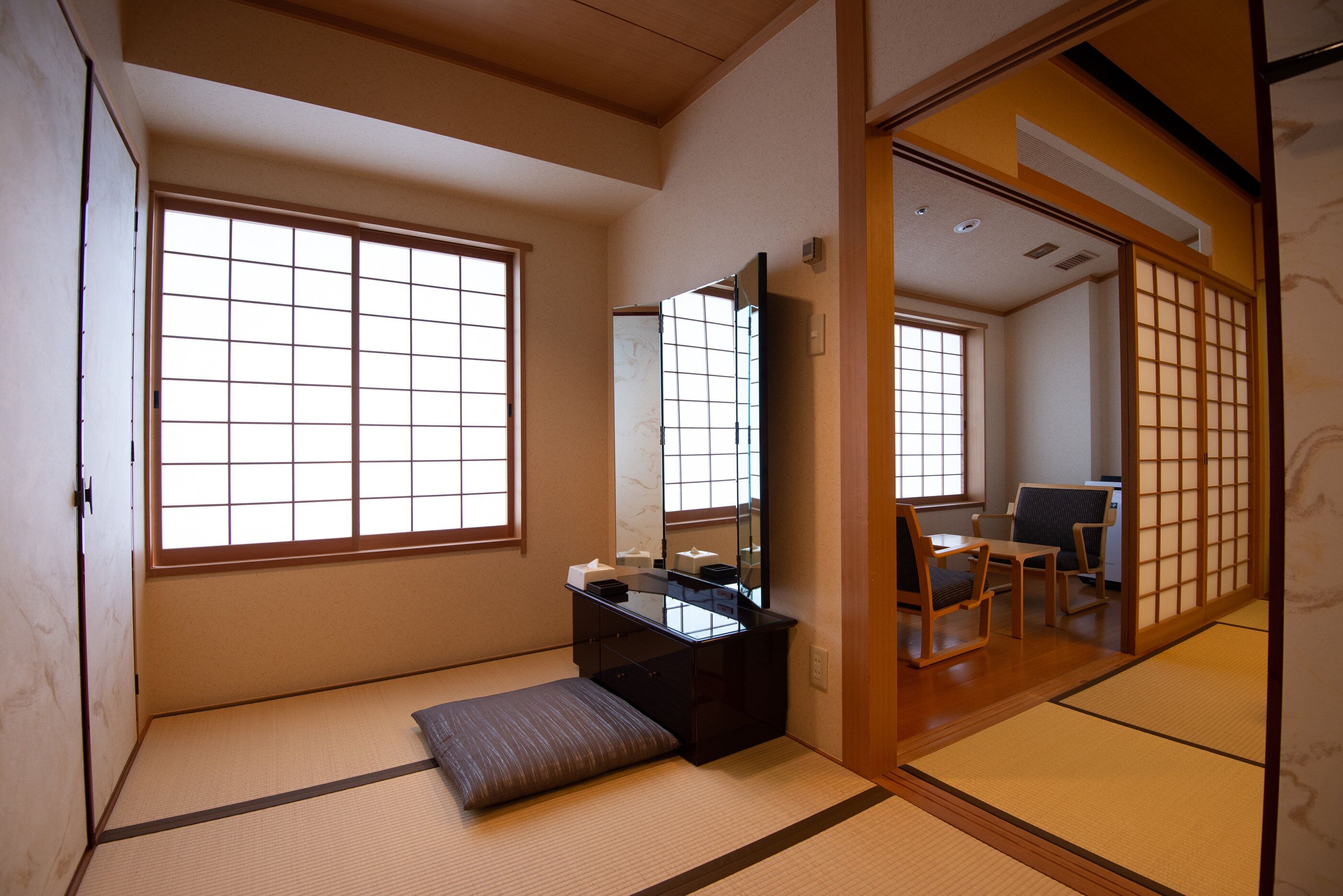 Una habitación japonesa tradicional con suelo de tatami, un escritorio de madera bajo, un banco acolchado y puertas correderas.