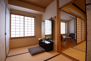 Una habitación japonesa tradicional con suelo de tatami, un escritorio de madera bajo, un banco acolchado y puertas correderas.