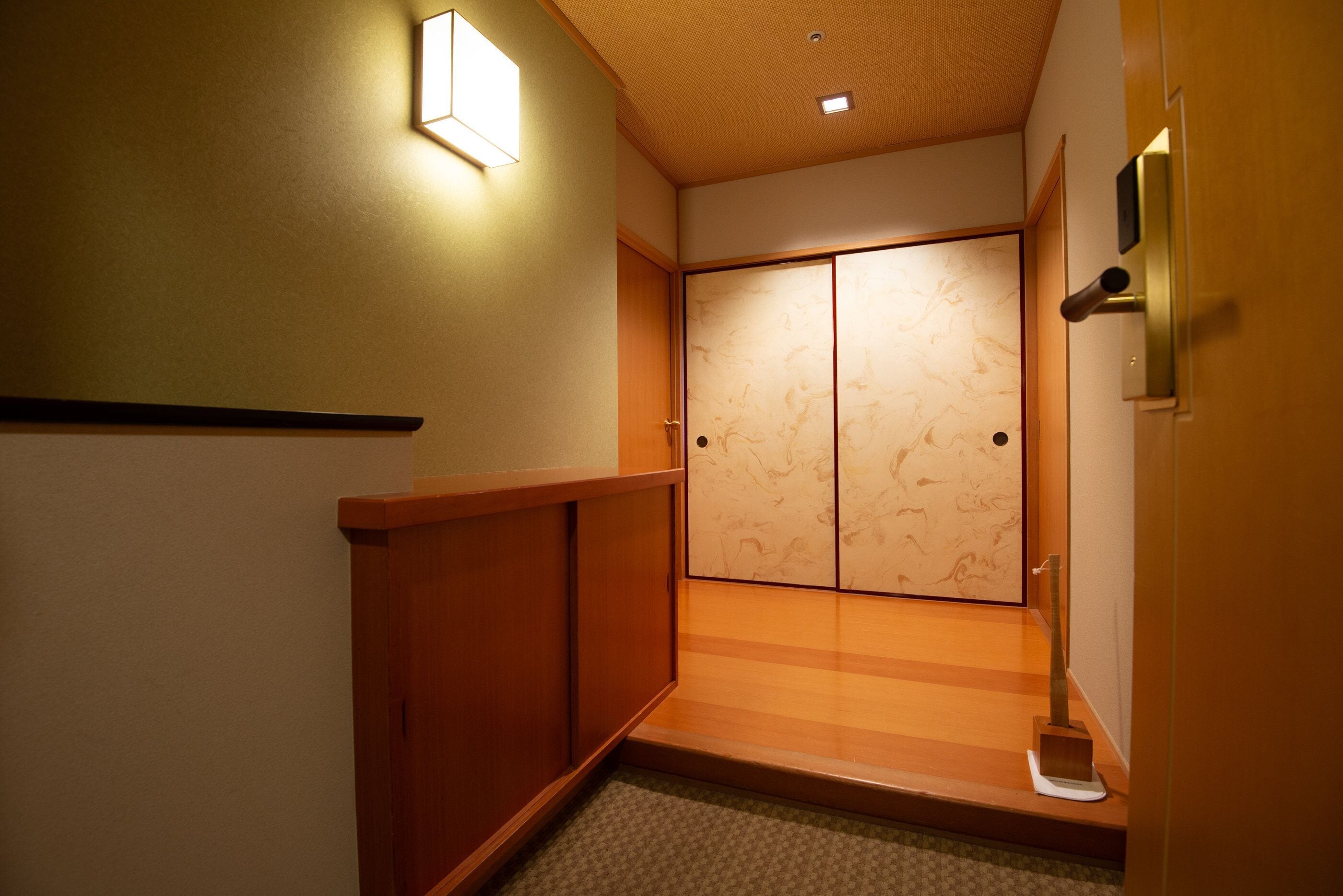 Una habitación japonesa tradicional con puertas correderas, suelo de madera y un pequeño escalón que conduce a la entrada.