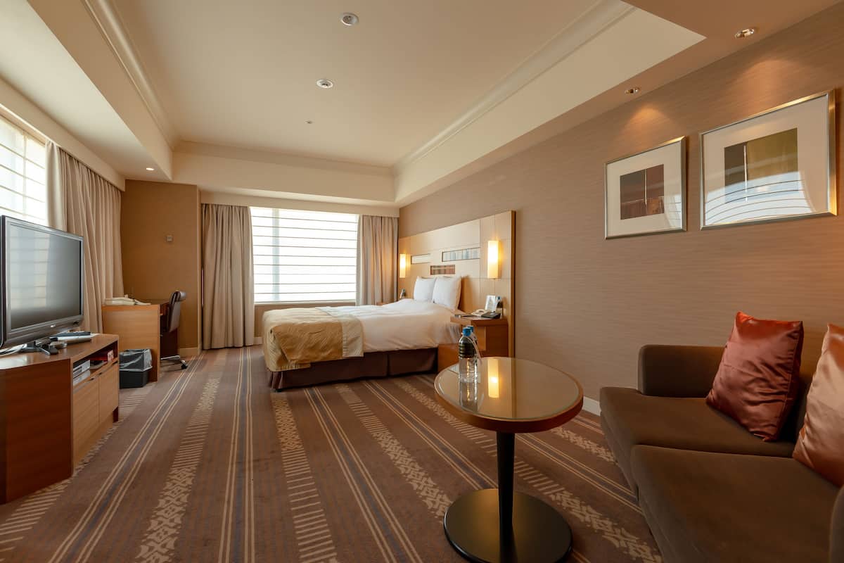 Une chambre d’hôtel avec un lit, une télévision, un bureau, un canapé et une petite table.