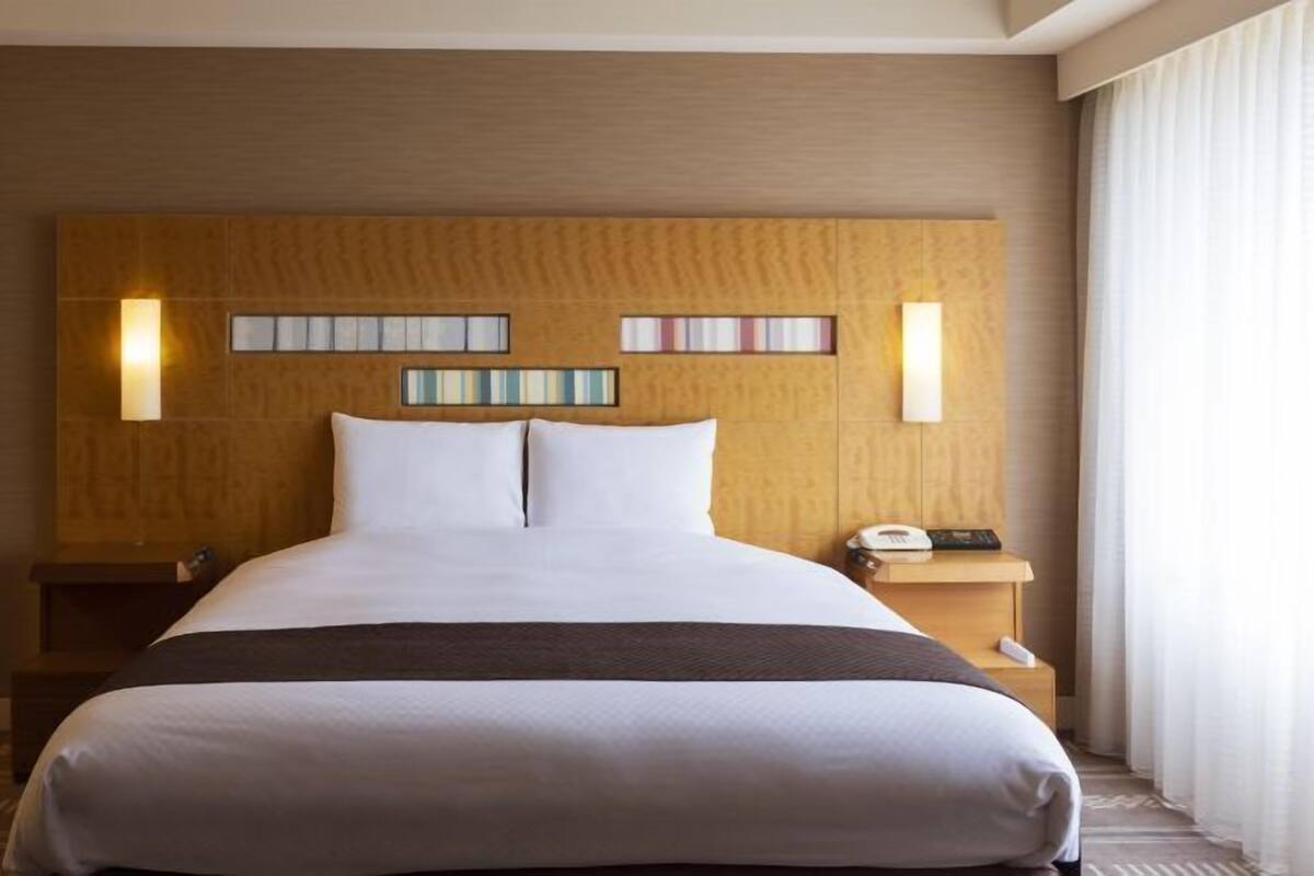 Une chambre d’hôtel avec un grand lit, une tête de lit en bois, des tables de chevet et une petite table de nuit avec un téléphone.