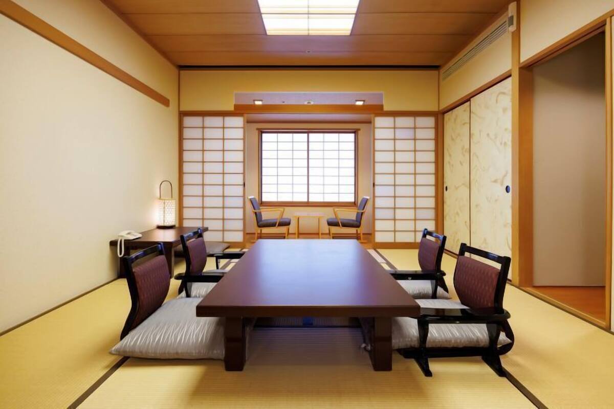 Une pièce de style japonais traditionnel, avec un sol recouvert de tatamis, une table basse, quatre chaises, une porte coulissante et une fenêtre ornée de panneaux shoji.