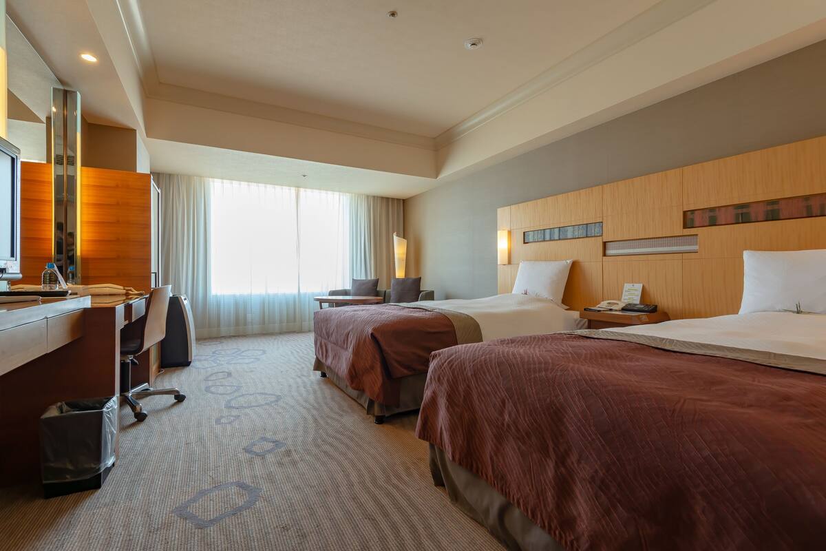 Une chambre d’hôtel avec deux lits, un bureau, une chaise et une poubelle.