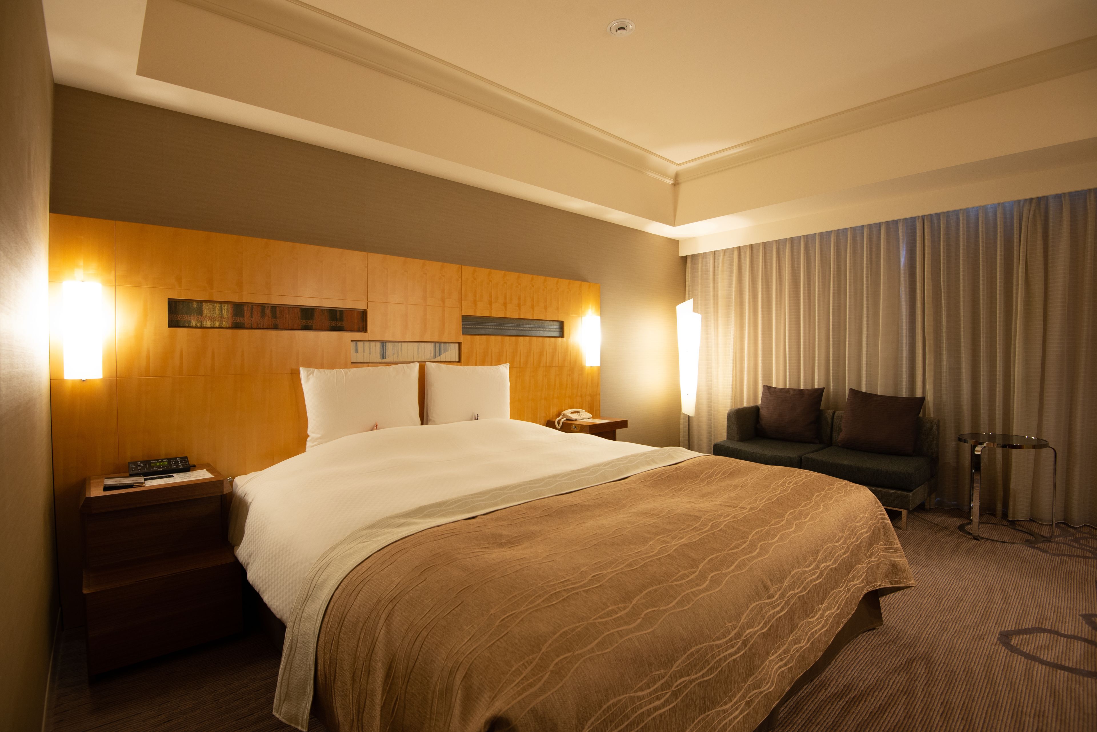 A hotel room with a large bed, a nightstand, a sofa, and a lamp.