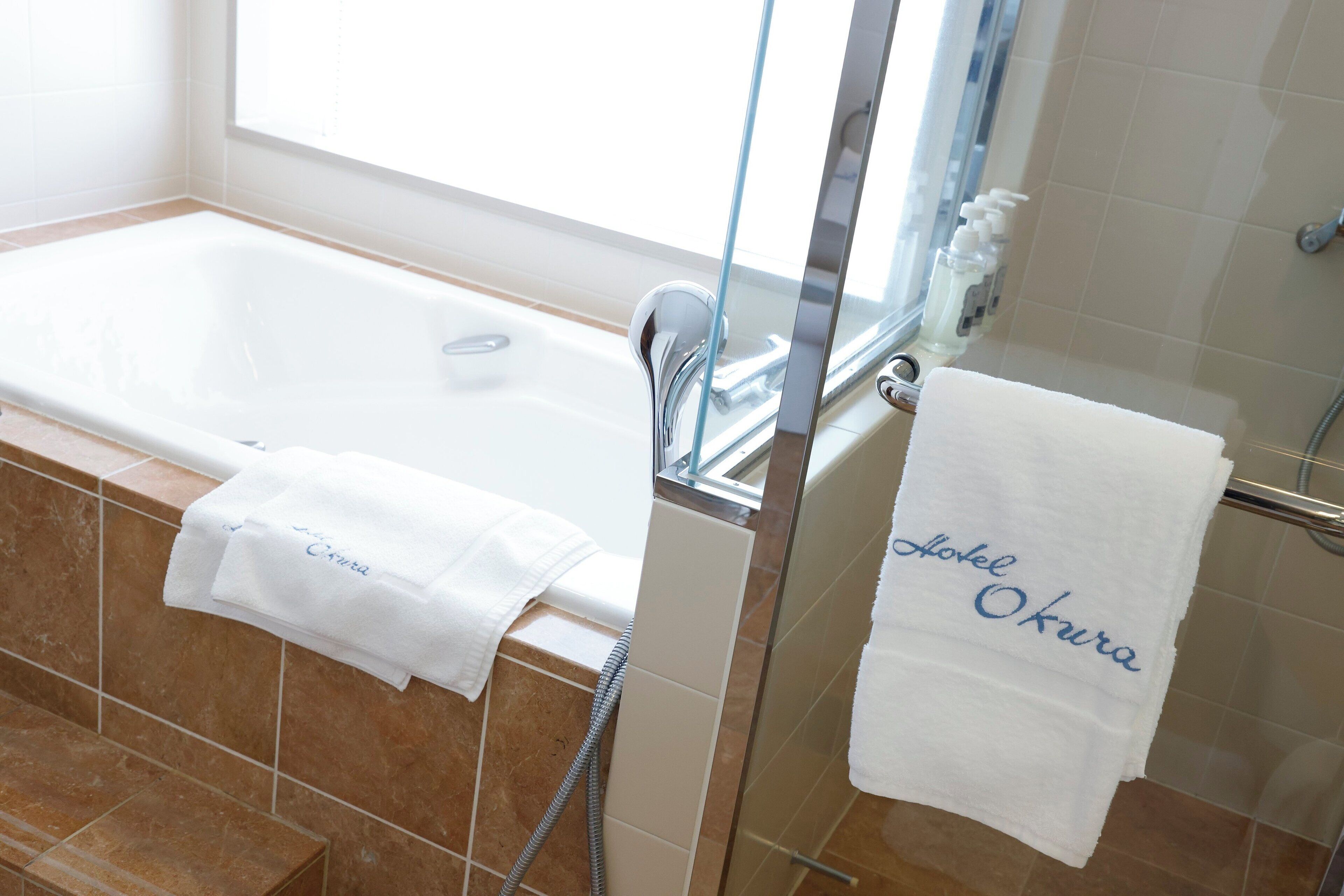 A bathroom with a bathtub, a glass shower enclosure, and two towels with text.