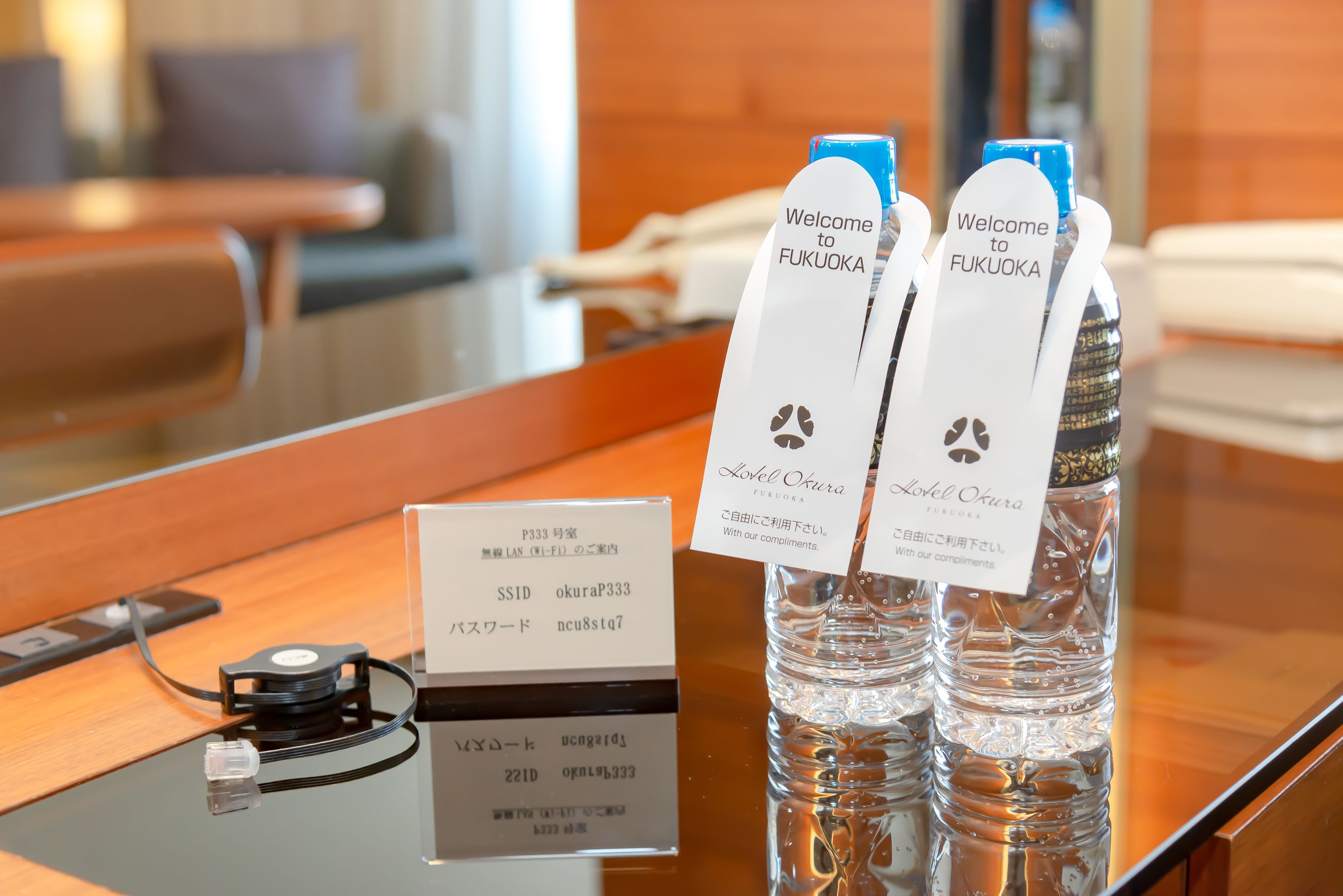 Una reception con un cartello che recita 'Welcome to Fukuoka' e due bottiglie d'acqua etichettate 'Lovely Okura'.