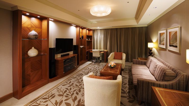 Ein Hotelzimmer mit Fernseher, Sofa, Sessel, Couchtisch und einer dekorativen Vase.