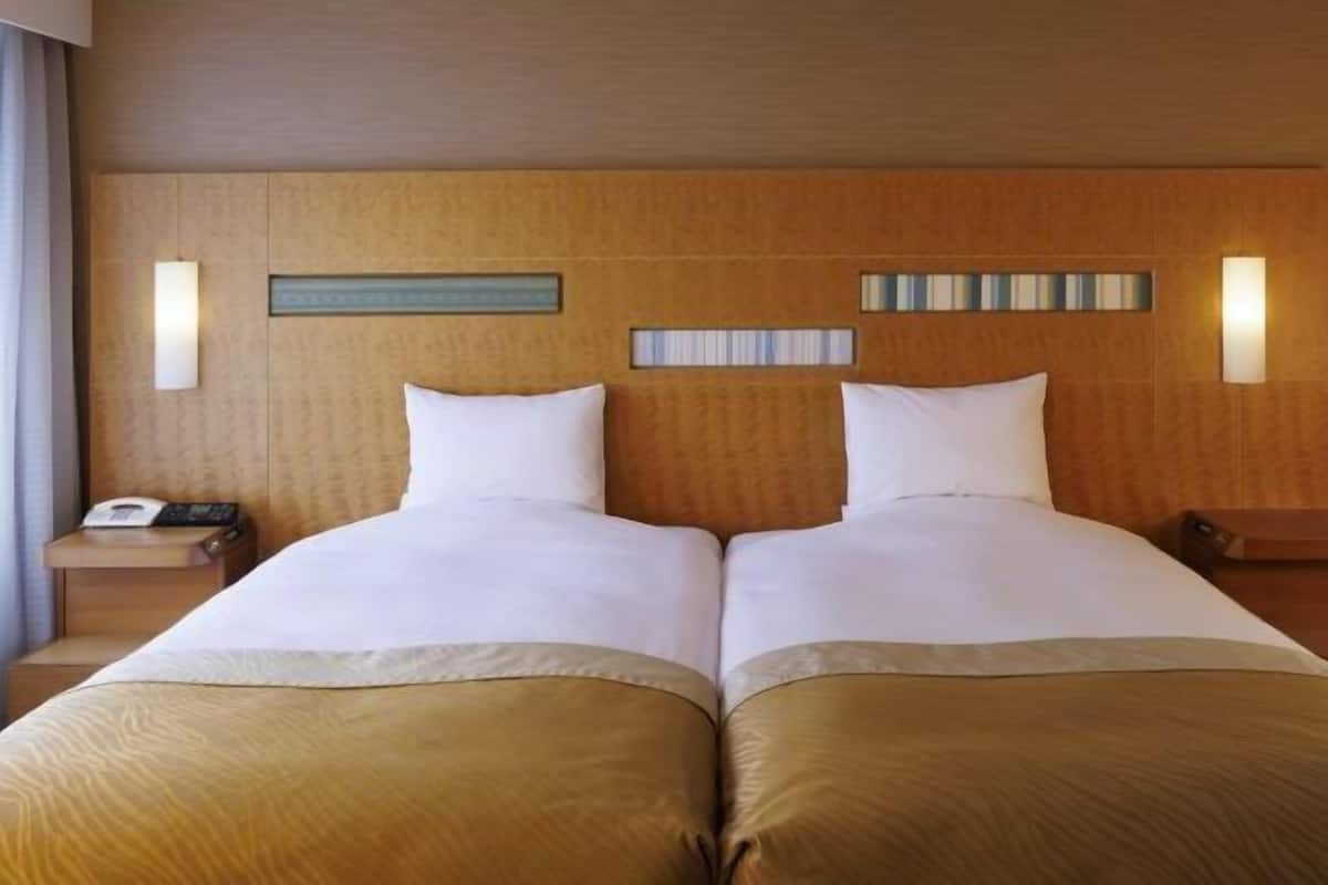 Une chambre double avec deux lits, une tête de lit en bois, des tables de chevet et un téléphone fixé au mur.
