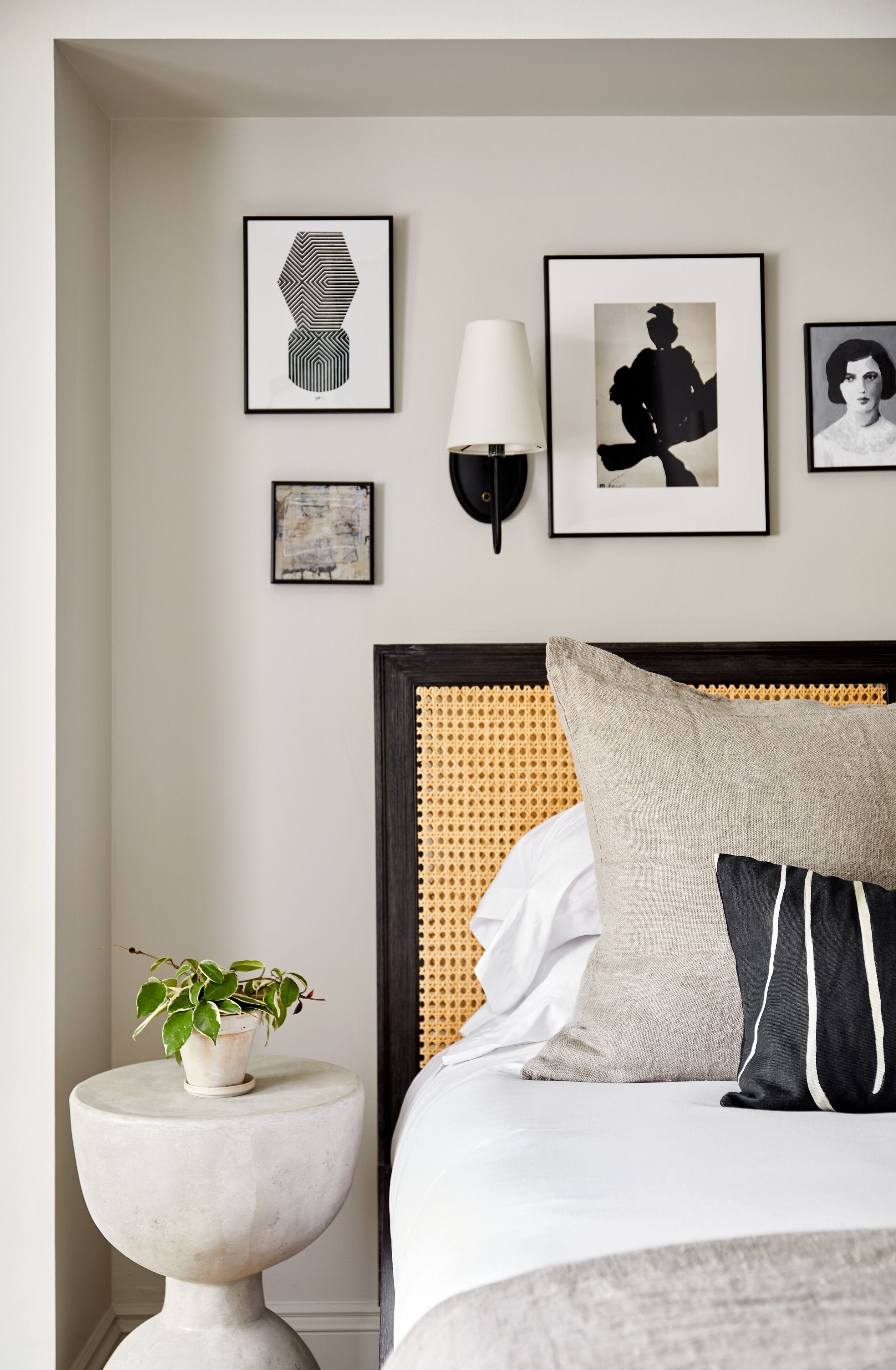 Quarto bem arrumado com uma cama, mesa de cabeceira com uma planta e quadros na parede.