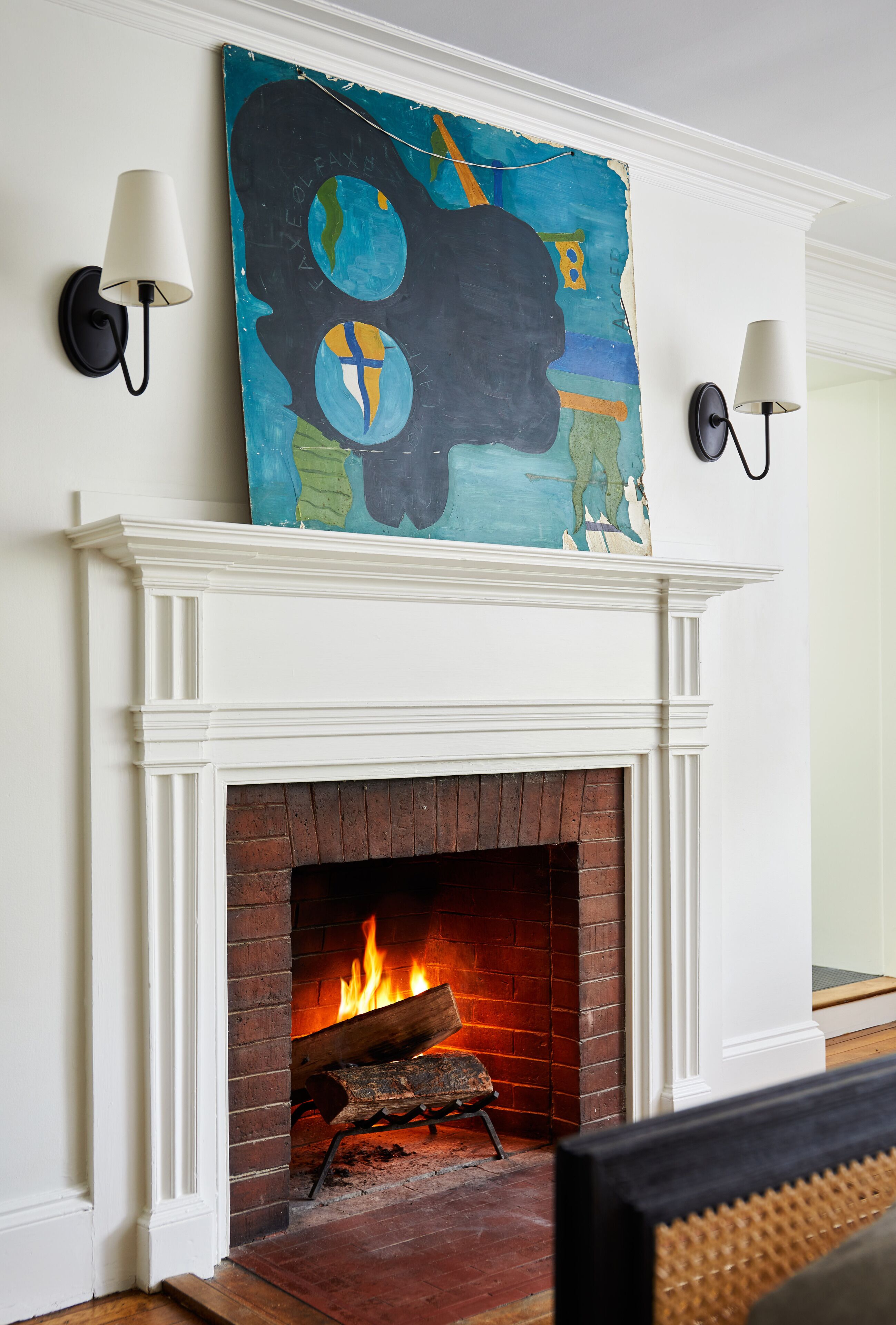 A fireplace with a burning log, a white mantel, and a large abstract painting above it.
