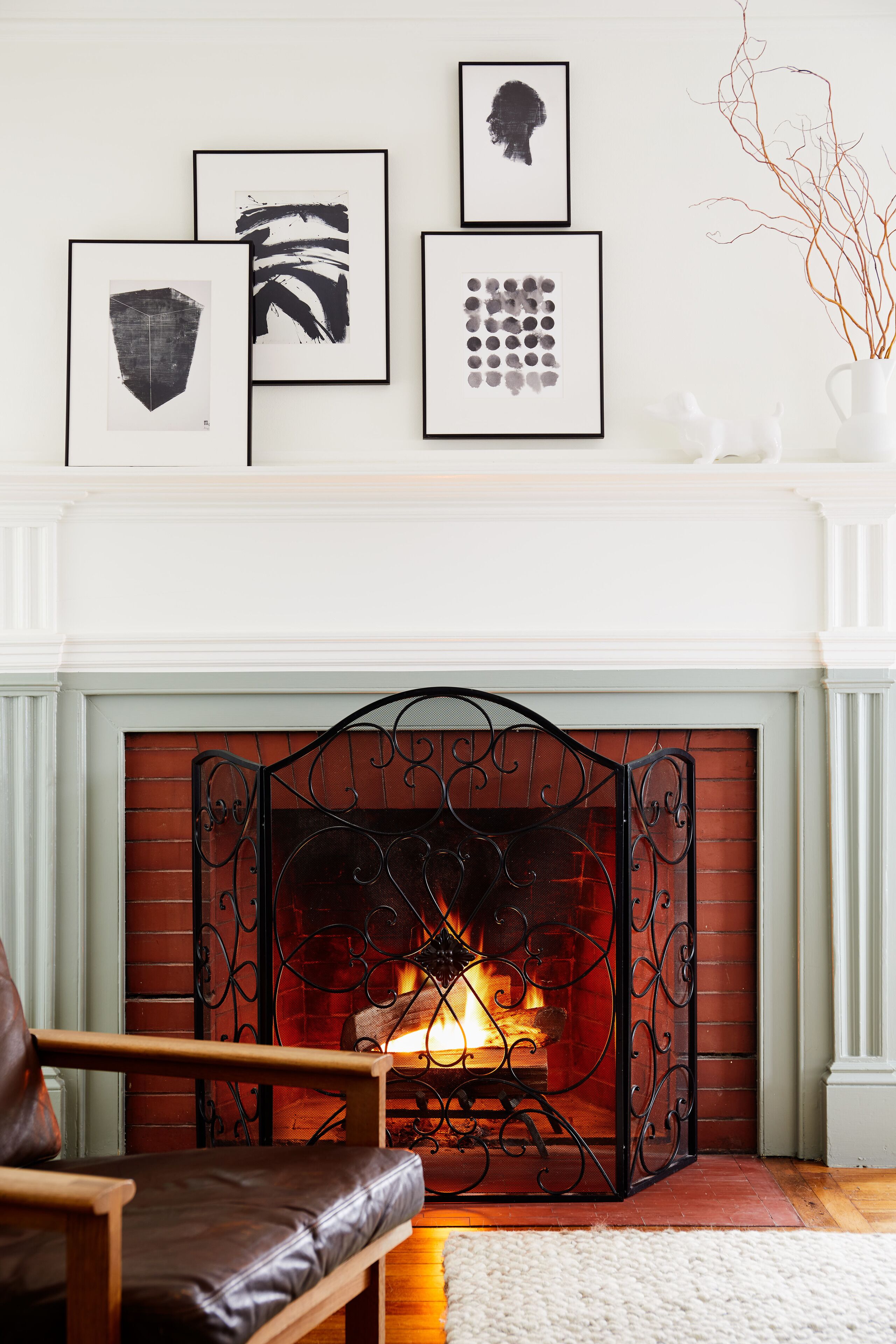 A fireplace with a brick surround, a framed artwork collection above it, and a leather chair in front.