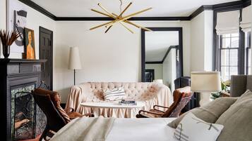 Une pièce bien éclairée, avec un canapé capitonné, une table ronde et un lit doté d’une tête de lit blanche.