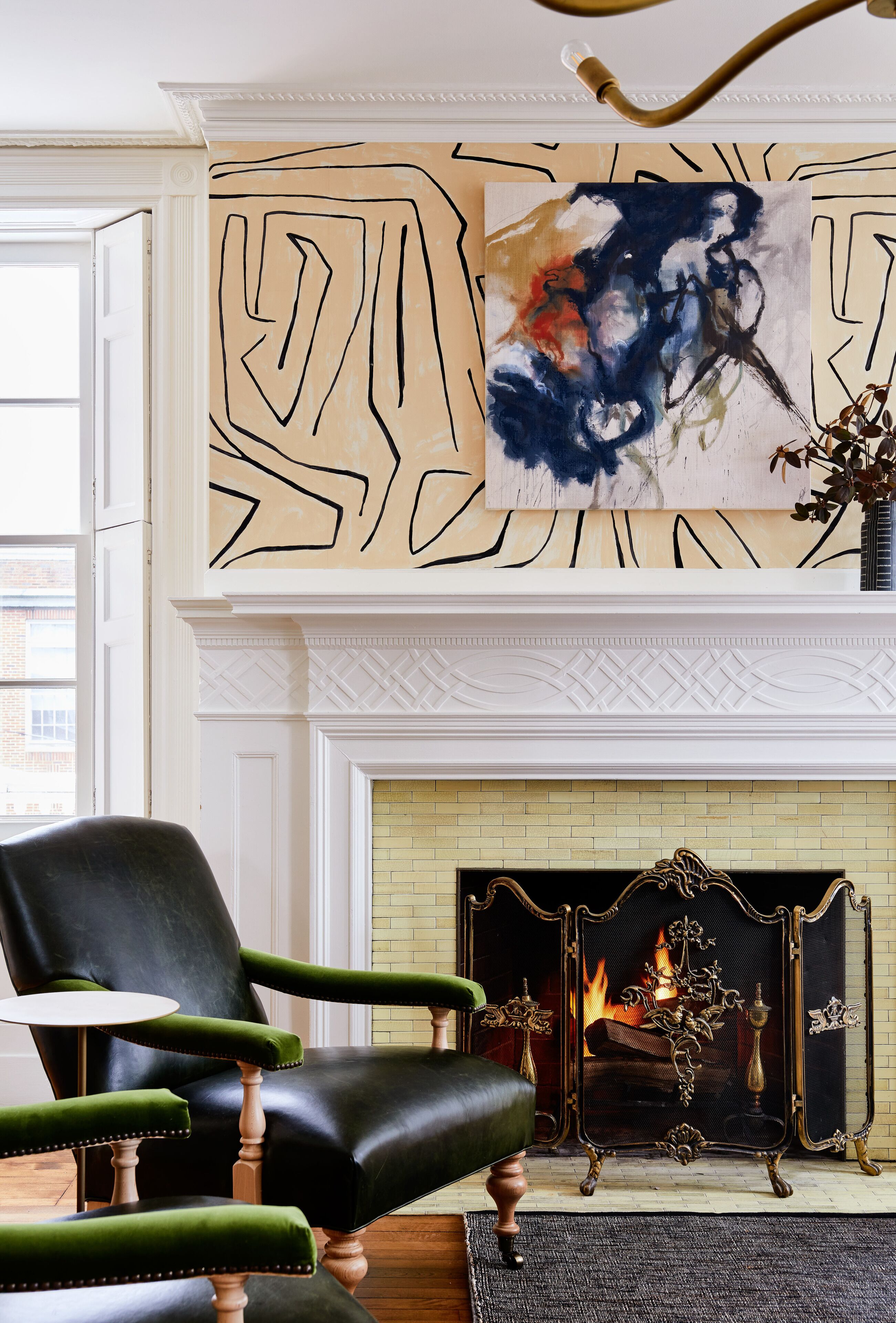 Une pièce avec une cheminée, un fauteuil vert et un grand tableau abstrait accroché au mur.