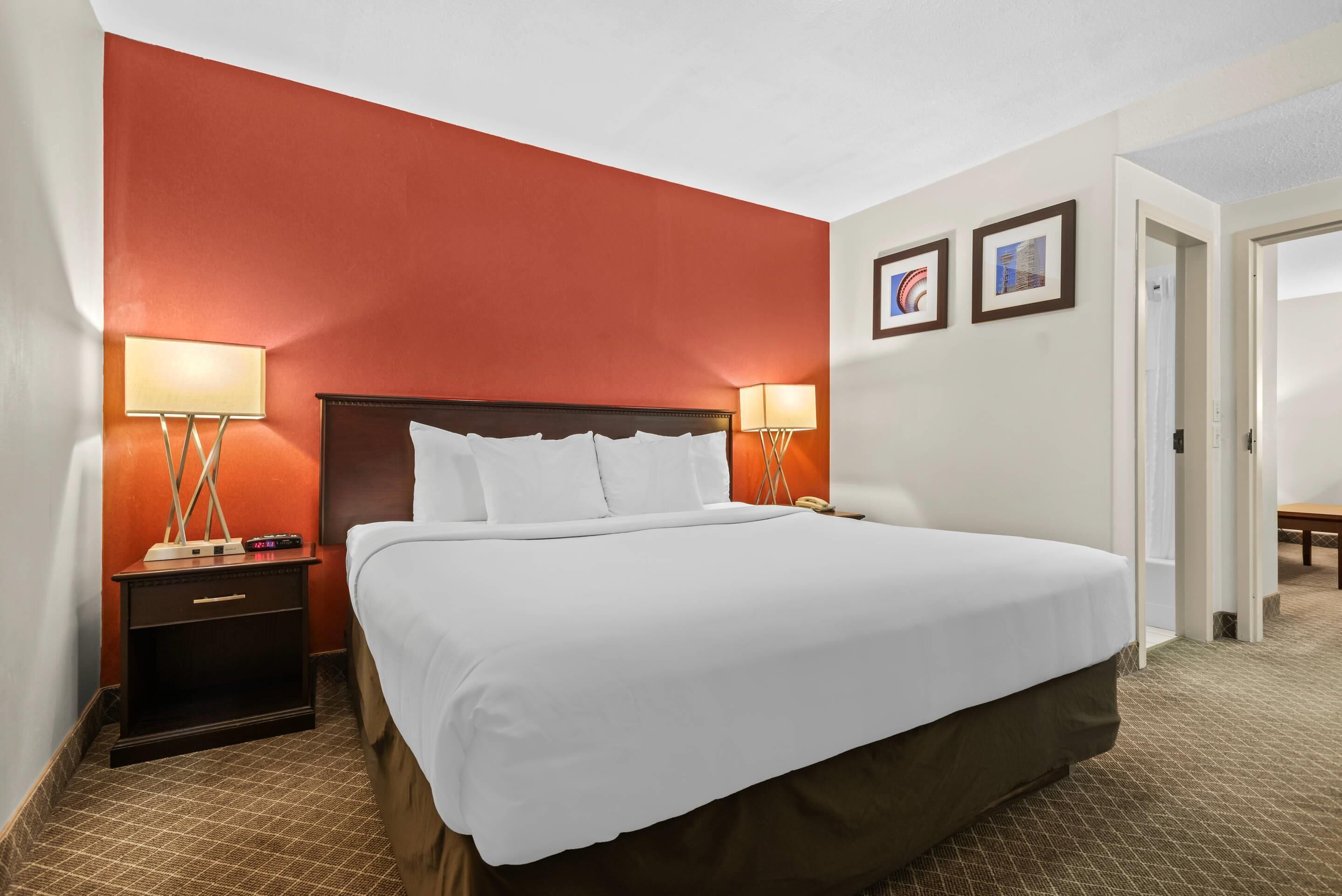 A hotel room with a large bed, two bedside lamps, a nightstand, and a door leading to another room.